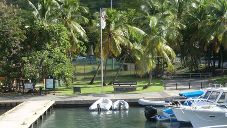 A dock with boats next to a park with palm trees and a sign reading “Virgin Islands National Park”