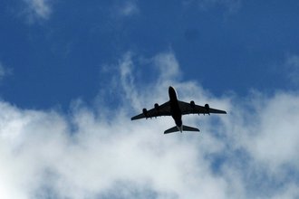 Photo of an airplane flying in a blue sky with light clouds.