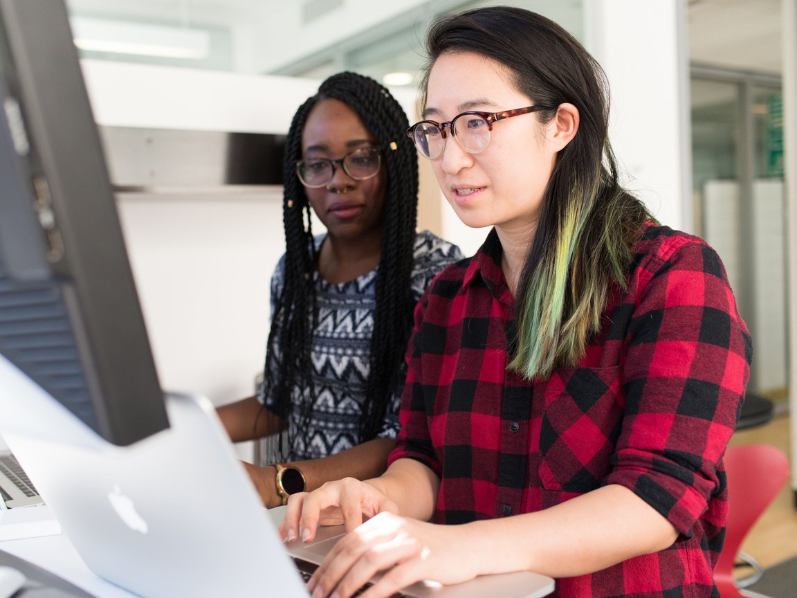 Two women in front of their computers, sharing a desk.