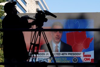 A shadow of a camera man against the background of a large television, showing the projected electoral map of the United States on CNN with Jake Tapper.