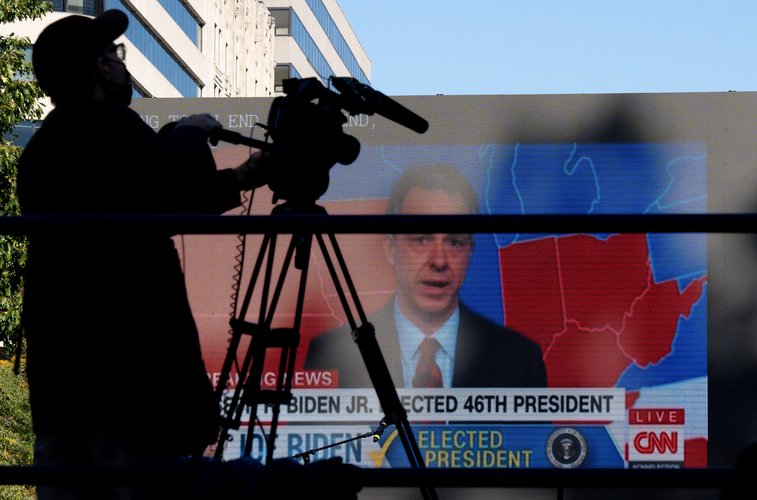 A shadow of a camera man against the background of a large television, showing the projected electoral map of the United States on CNN with Jake Tapper.