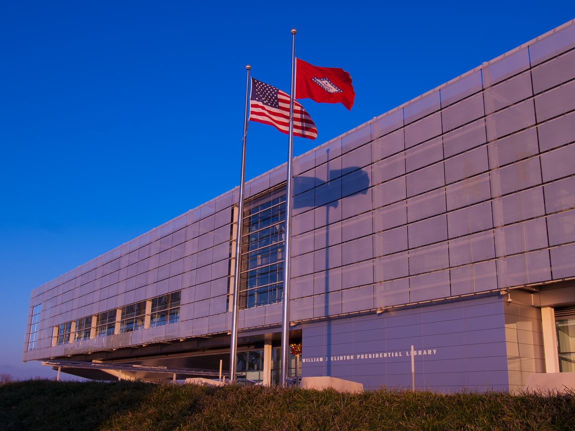 The Clinton presidential library at sunset, with two flag poles flying the U.S. and Arkansas state flags in front of the building