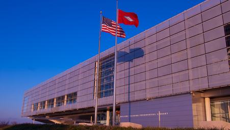 The Clinton presidential library at sunset, with two flag poles flying the U.S. and Arkansas state flags in front of the building