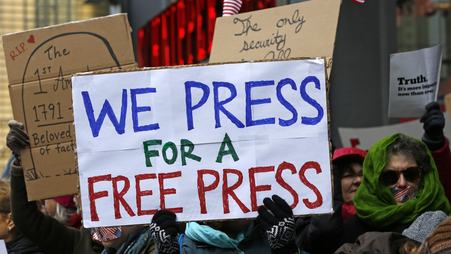 A group of protesters hold signs in solidarity with the press in February 2017; one says, “We press for a free press”