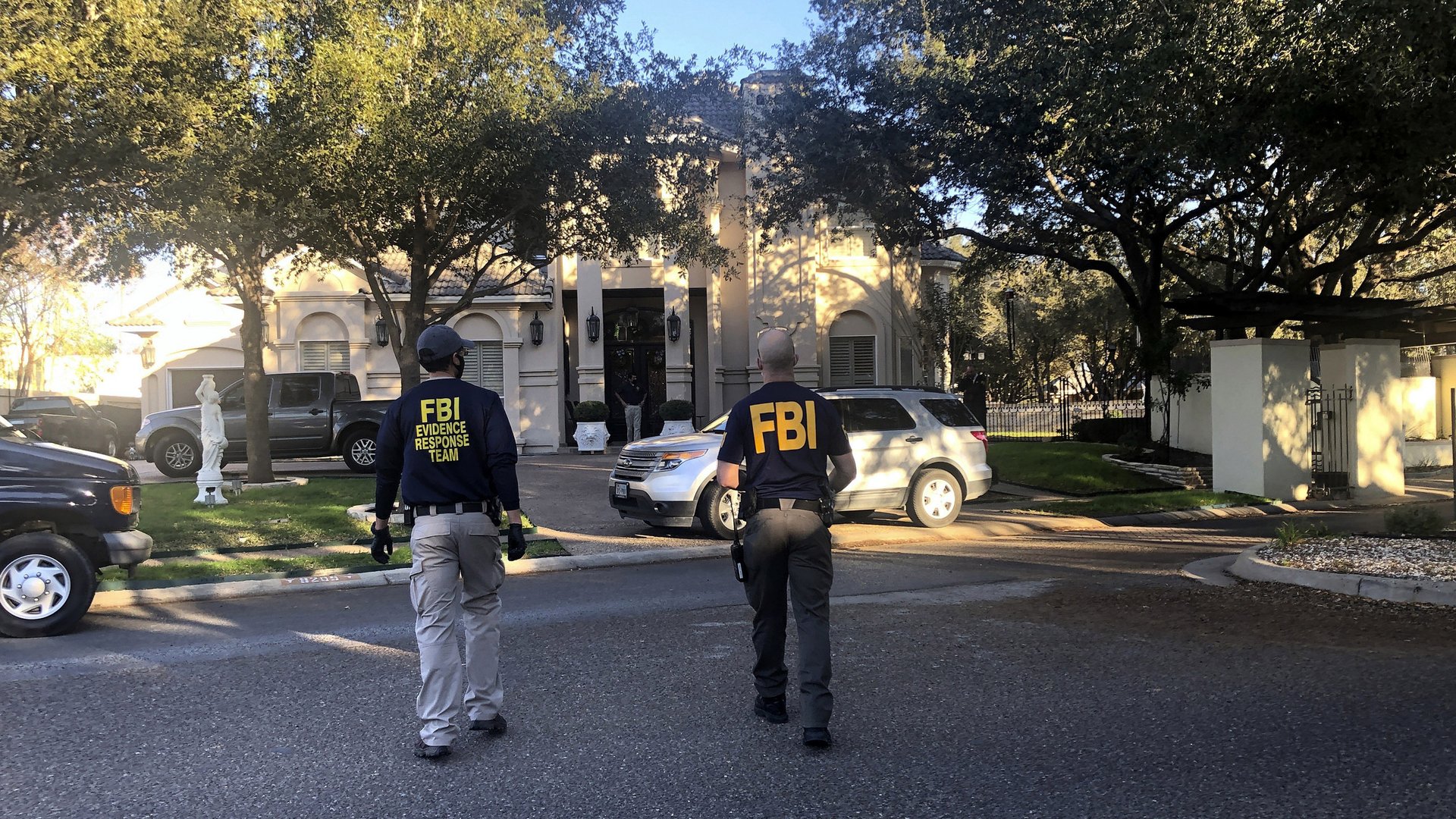 Two federal agents, wearing shirts with “FBI” on the back, walk in a street.
