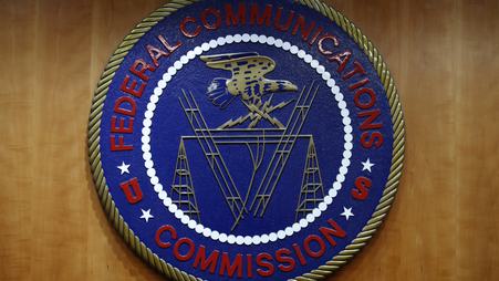Image of the FCC seal: a blue emblem with the words “Federal Communications Commission” in red with an eagle in the center flying over images of communications technology.