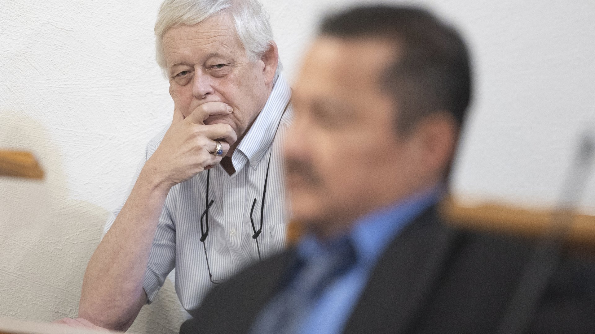 A photograph of man in the background looks forward toward a man in the foreground who is out of focus.