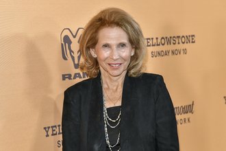 Paramount Global Chair Shari Redstone pictured in a black shirt and blazer in front of an orange-tan background