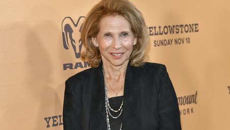 Paramount Global Chair Shari Redstone pictured in a black shirt and blazer in front of an orange-tan background