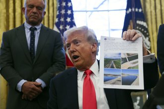 President Donald Trump holds up a printout of a Truth Social post.