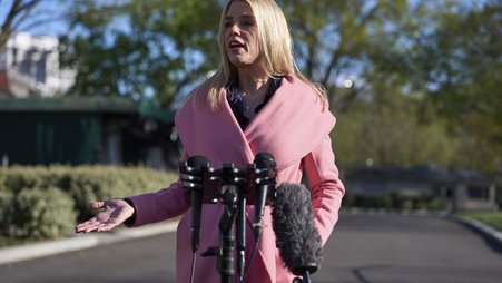 Attorney General Pam Bondi talking to reporters in a pink coat.