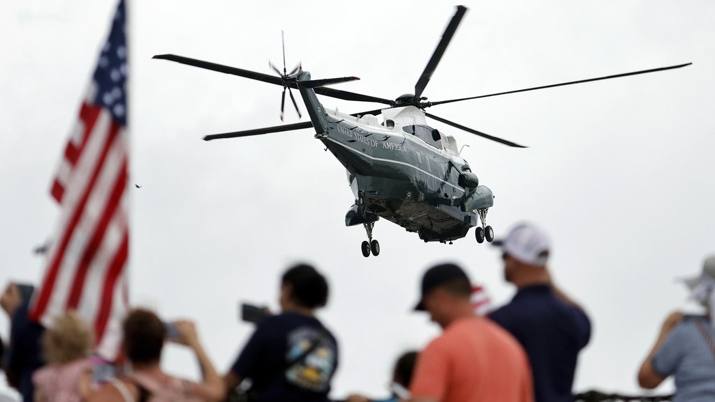 President Donald Trump’s helicopter flies away, with blurred images of people and an American flag in the foreground.