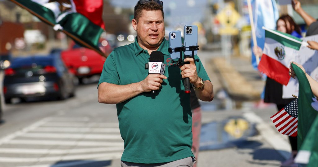 A man is standing in the street livestreaming with two phones and a microphone