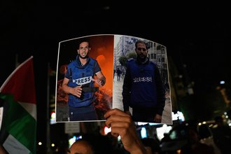 A photo of a protester's hand holding a placard on which two Palestinian journalists are pictured.