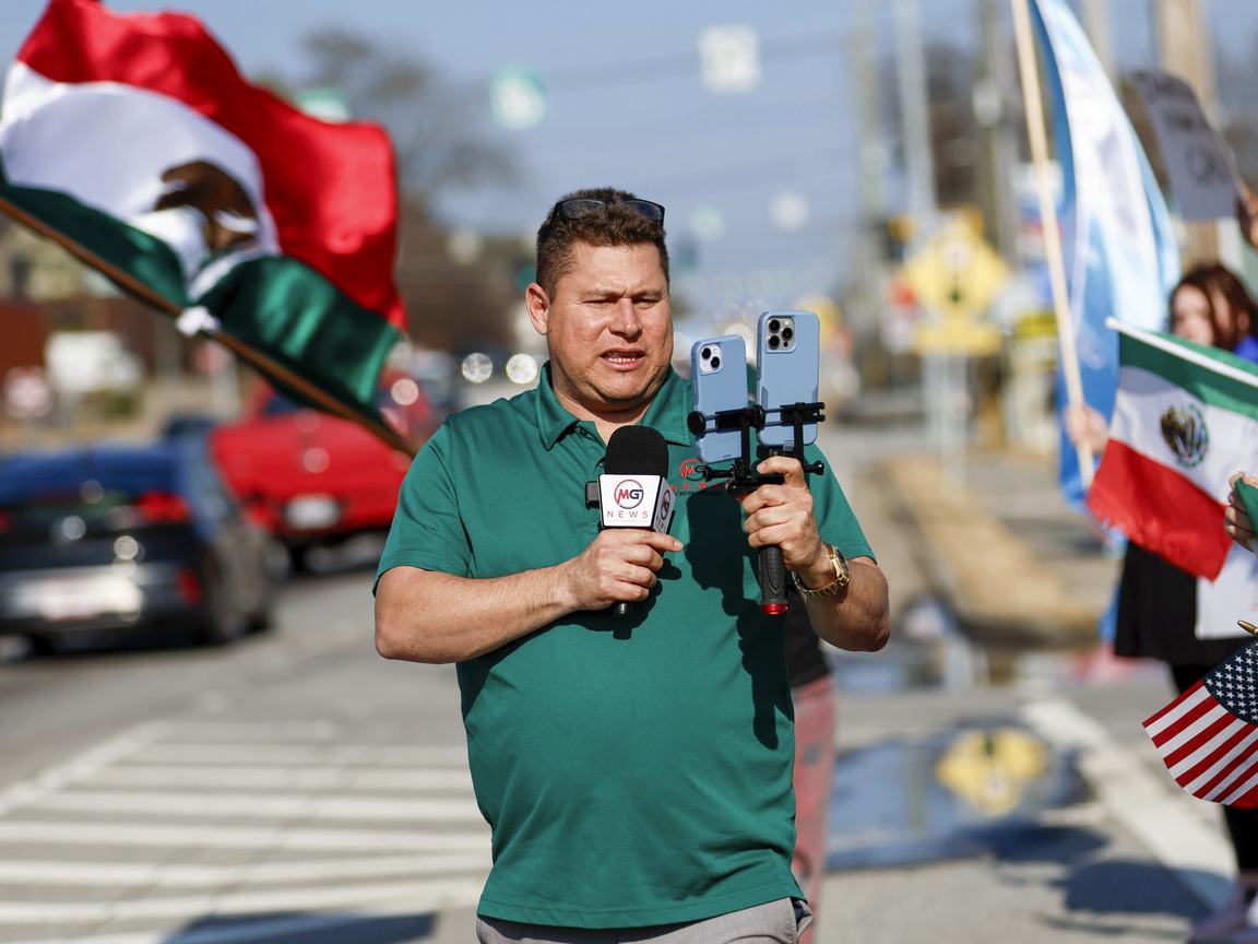 Journalist Mario Guevara, in a green shirt, stands in the street livestreaming with two phones and a microphone
