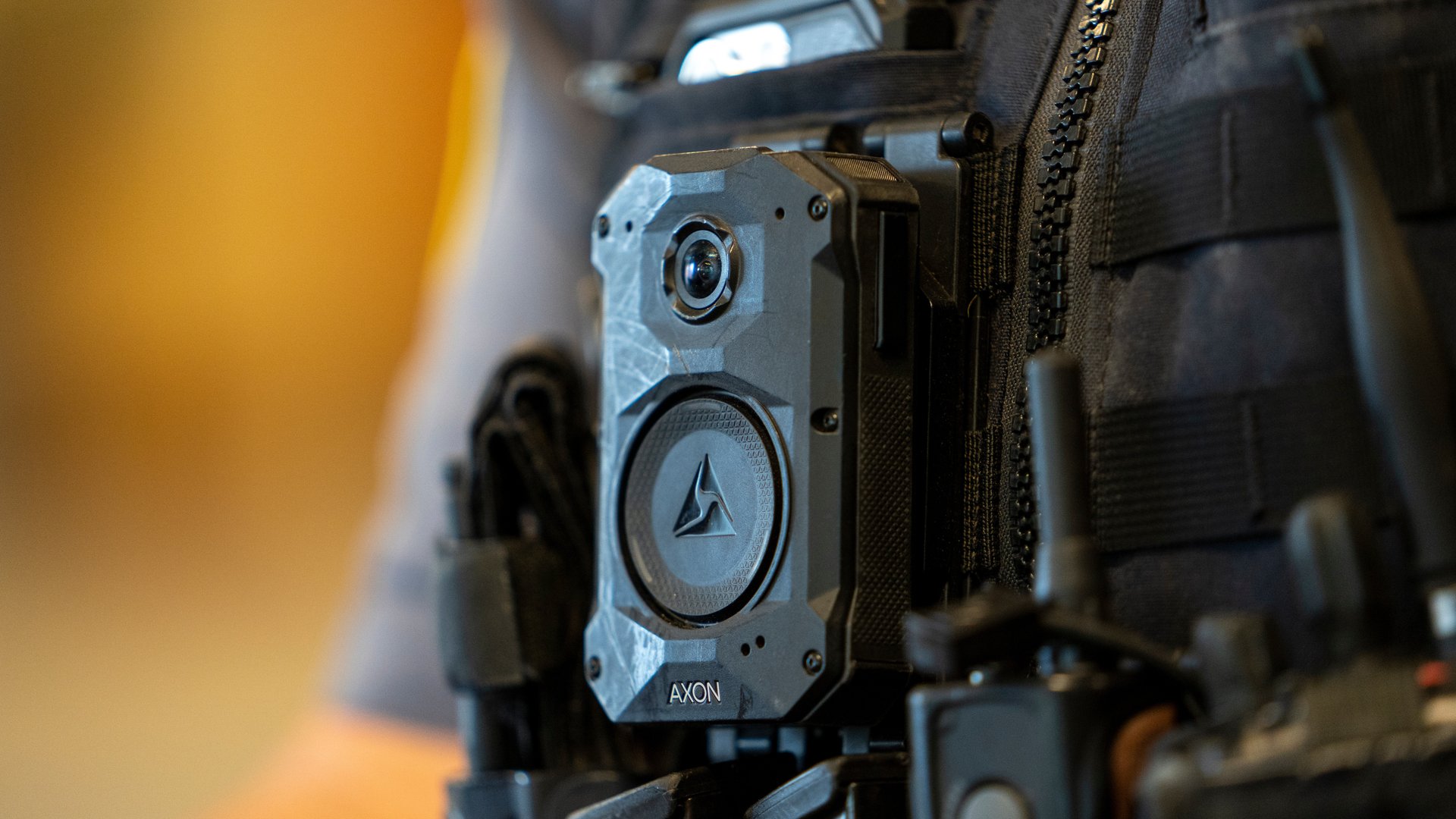 A close up photo of an Axon-brand body camera on the vest of a police officer.