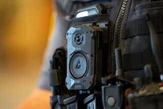 A close up photo of an Axon-brand body camera on the vest of a police officer.