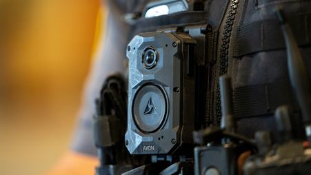 A close up photo of an Axon-brand body camera on the vest of a police officer.