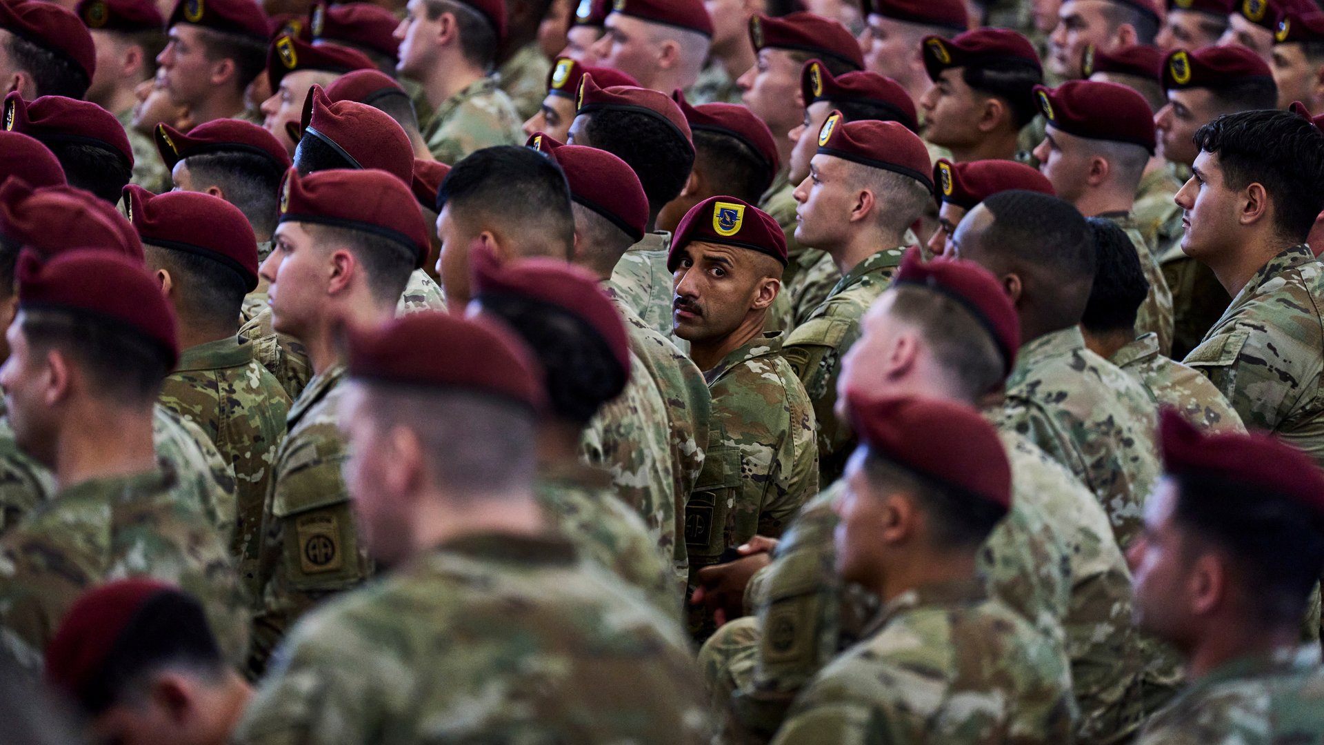 A group of men in camouflage and red berets, facing forward; one is turned to look at the photographer