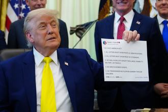 President Donald Trump in the Oval Office holds up a printout of one of his Truth Social posts in June 2026.
