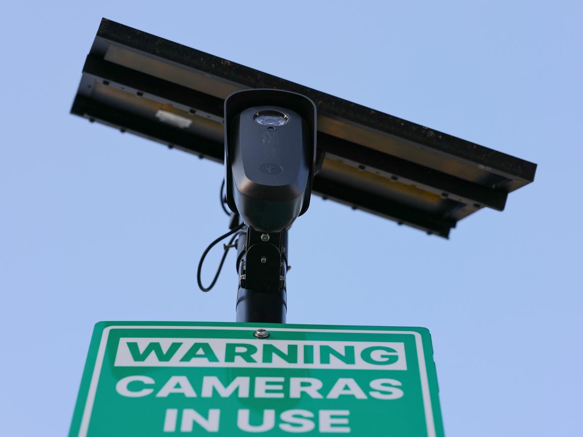 A camera mounted to a pole appears above a sign that reads: “WARNING CAMERAS IN USE”