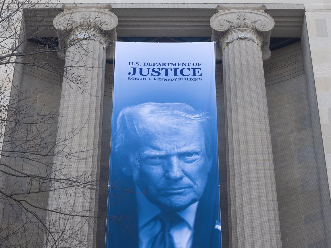 A banner with an image of President Donald Trump hangs outside Department of Justice headquarters in Washington, D.C. on March 11, 2026