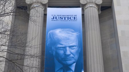 A banner with an image of President Donald Trump hangs outside Department of Justice headquarters in Washington, D.C. on March 11, 2026