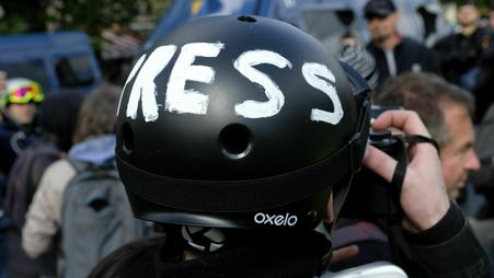 A person, seen from behind with a close-up on their head, takes a picture while wearing a black helmet with the word PRESS written in white across it.