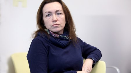 Alsu Kurmasheva, wearing a blue sweater and scarf, sits facing the camera and looking into the distance
