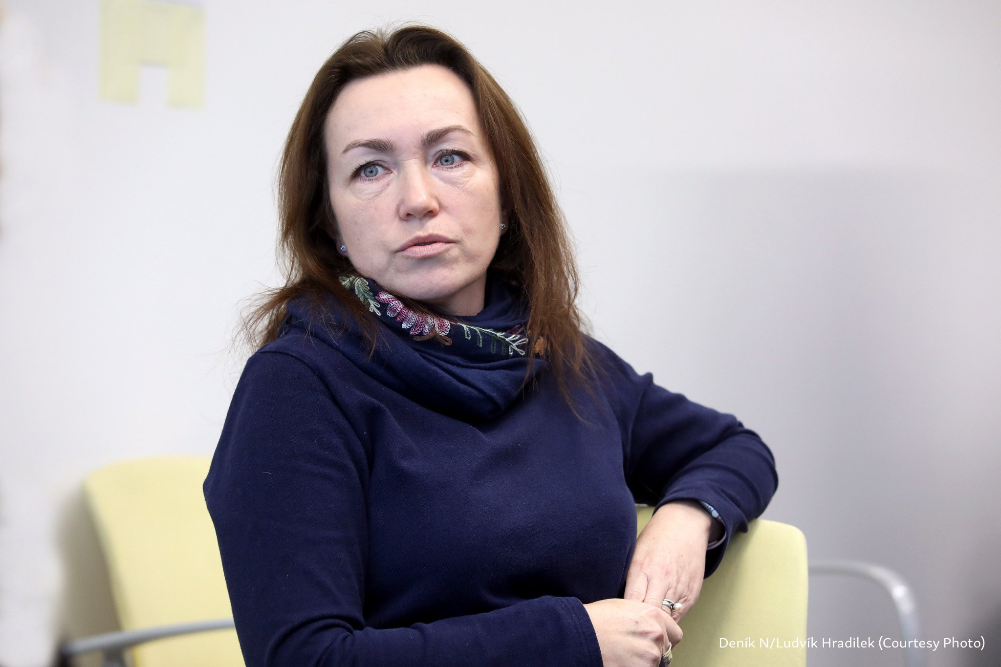 Alsu Kurmasheva, wearing a blue sweater and scarf, sits facing the camera and looking into the distance