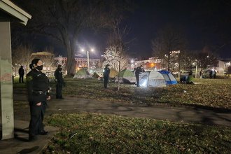 Several police officers stand in a field with tents at night time.