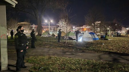 Several police officers stand in a field with tents at night time.