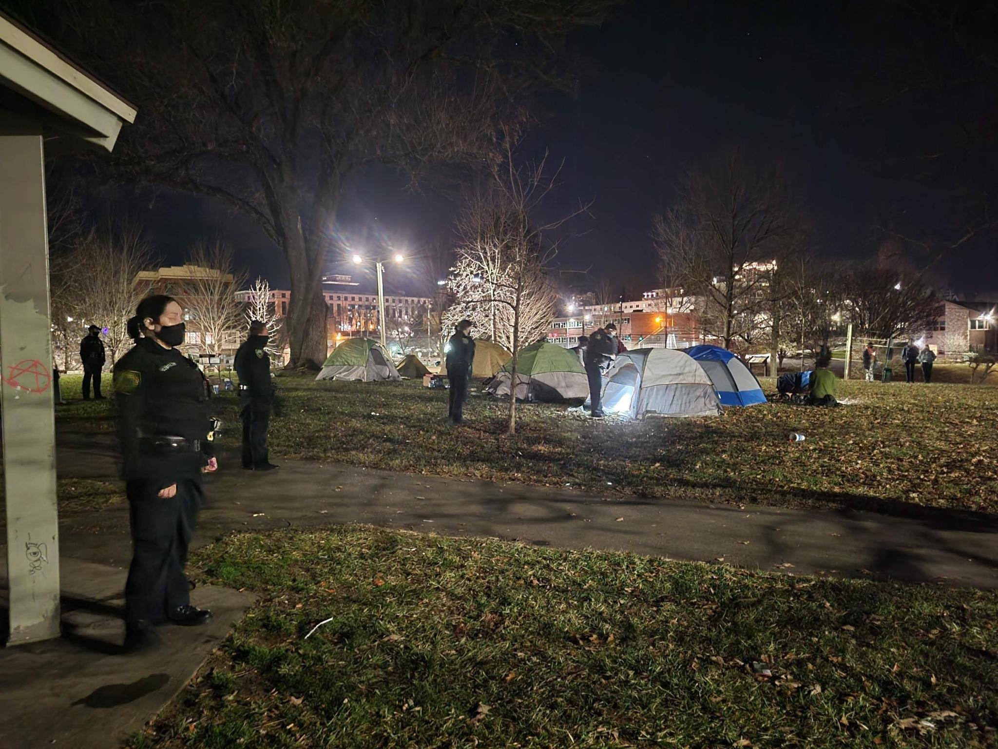 Several police officers stand in a field with tents at night time.