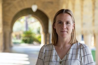 Hannah Bassett stands under building arches on the Stanford campus.