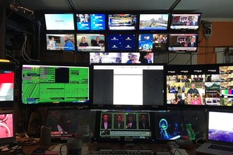 A bank of television and computer screens sits in a dark room