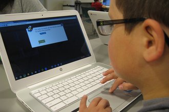A child wearing glasses looks at a computer screen.
