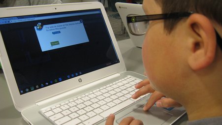 A child wearing glasses looks at a computer screen.