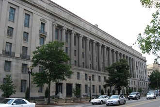 A stone government building with columns on a tree-lined street
