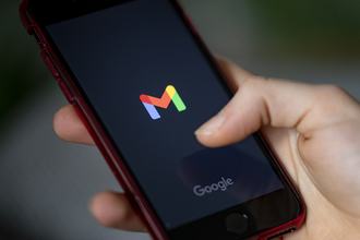 A hand holds a smartphone showing the logo of the Gmail app and the word “Google” on the screen.