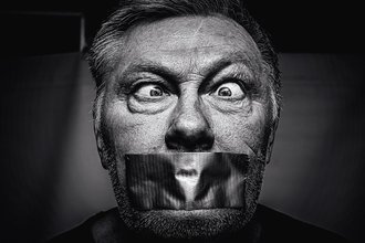 Close up on the face of a man crossing his eyes and with duct tape over his mouth