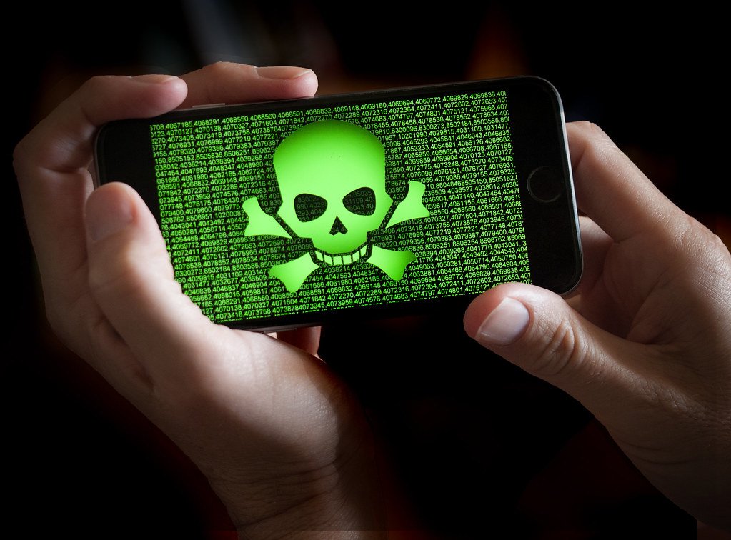 A person holds a phone displaying a green skull and crossbones and strings of numbers.