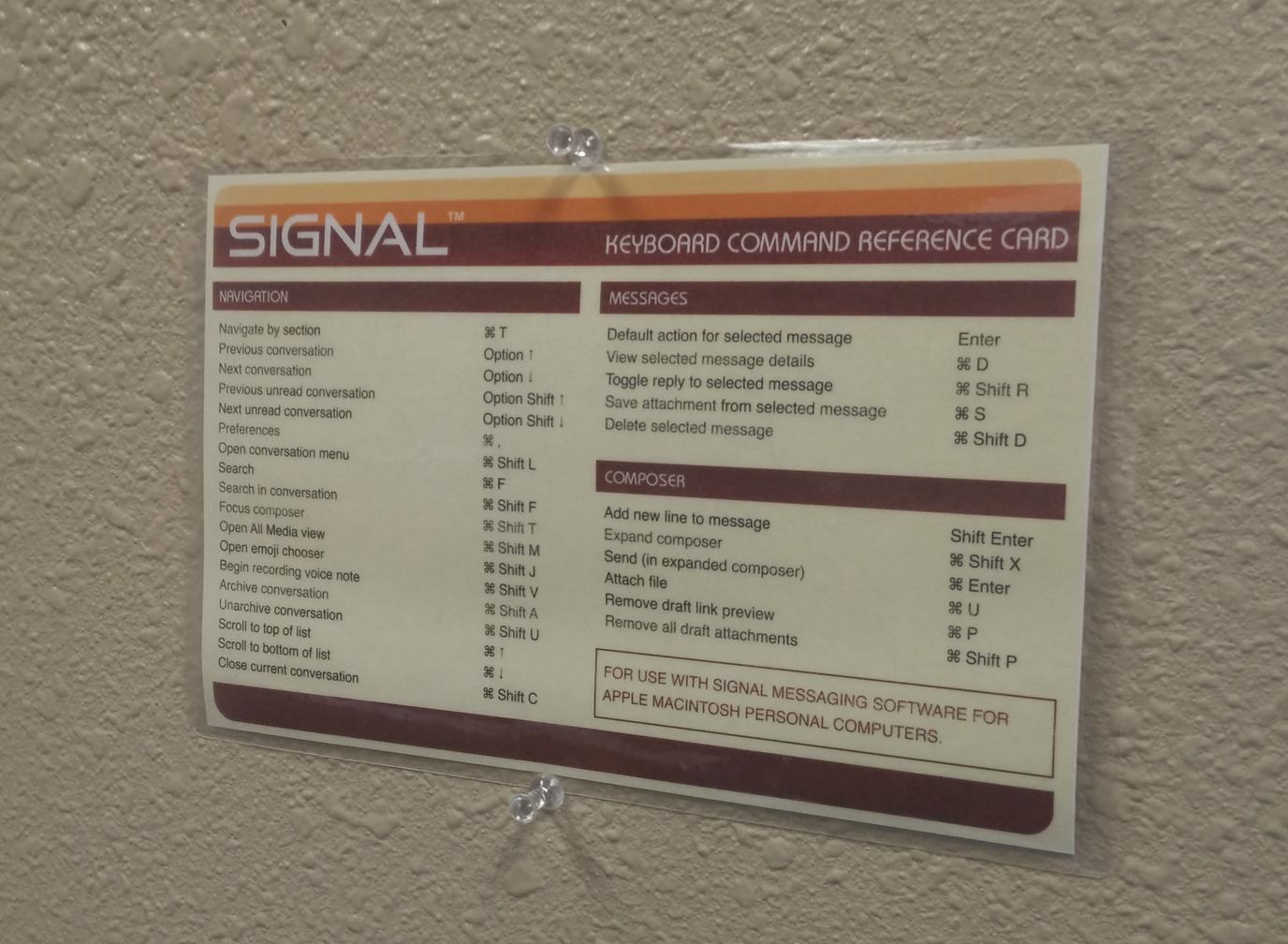 A Signal "reference card" with shortcut commands, pinned to the wall.