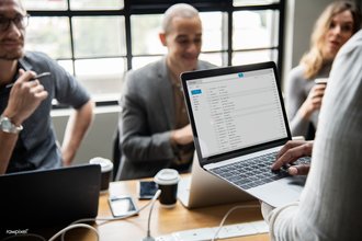 A person holds a laptop displaying email, with his hand resting on the keyboard, as three other people look on.