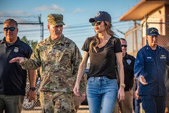A photo of DHS Secretary Kristi Noem walking alongside a uniformed member of the military.