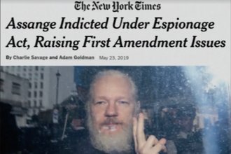 Picture of a New York Times headline reading, "Assange Indicted Under Espionage Act, Raising First Amendment Issues" above a picture of Assange with a white beard and holding up two fingers.