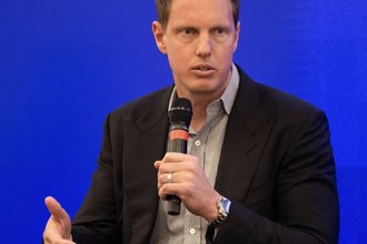 David Ellison pictured at a Paramount media event holding a microphone in front of a blue background