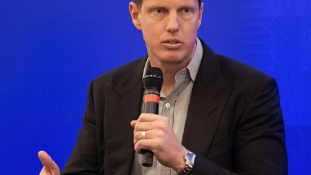David Ellison pictured at a Paramount media event holding a microphone in front of a blue background