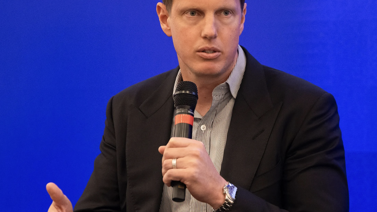 David Ellison pictured at a Paramount media event holding a microphone in front of a blue background