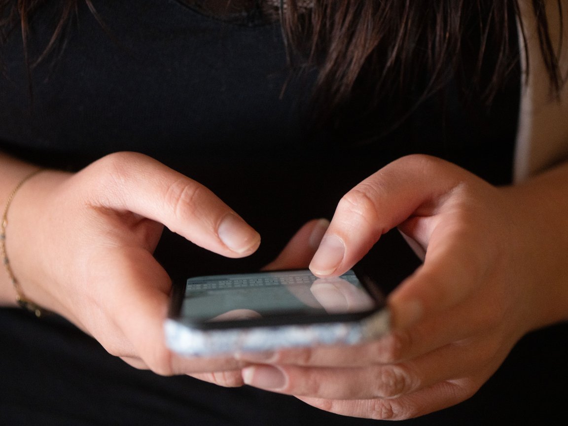 A woman types on a smartphone.