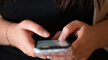 A woman types on a smartphone.